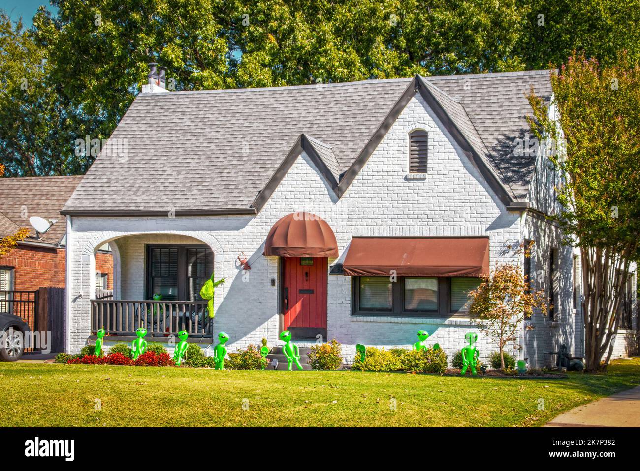 Grazioso cottage di mattoni dipinti di bianco con tende e rosso rustico porta decorata per Halloween con gonfiabili stranieri verdi - invasione da spazio esterno Foto Stock