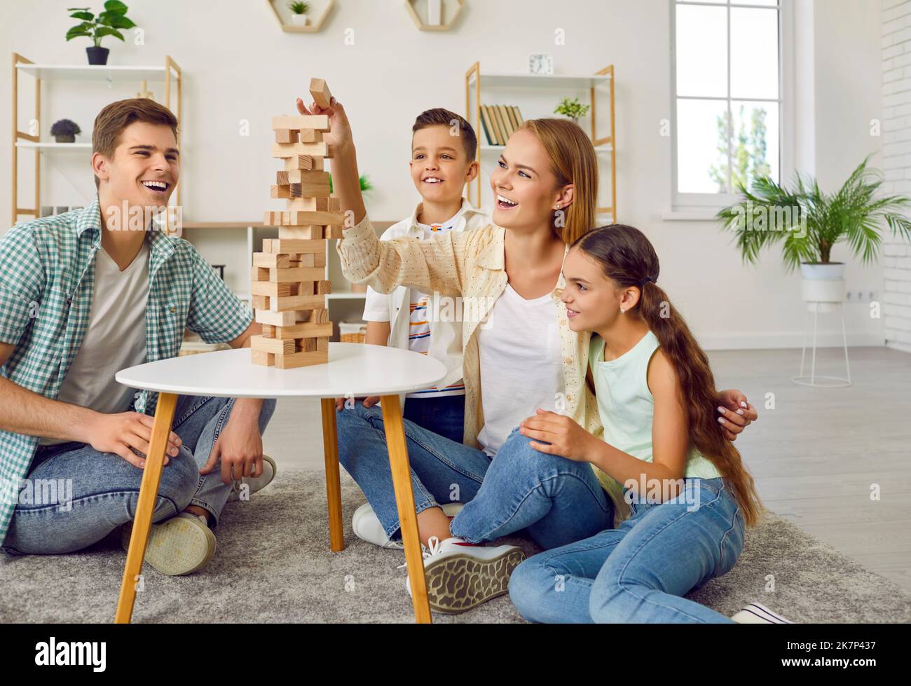 La famiglia felice con due bambini sta giocando la torre tumbling seduta sul pavimento nel paese. Foto Stock