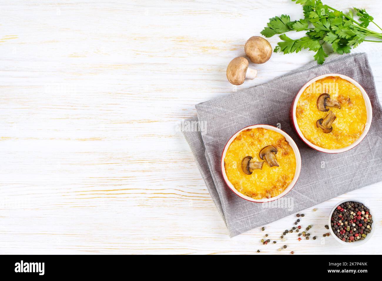Casseruola di pollo e funghi con crosta dorata, julienne con formaggio al forno, gratin cremoso in parte ramekin creta pentola su fondo di legno bianco. FR Foto Stock