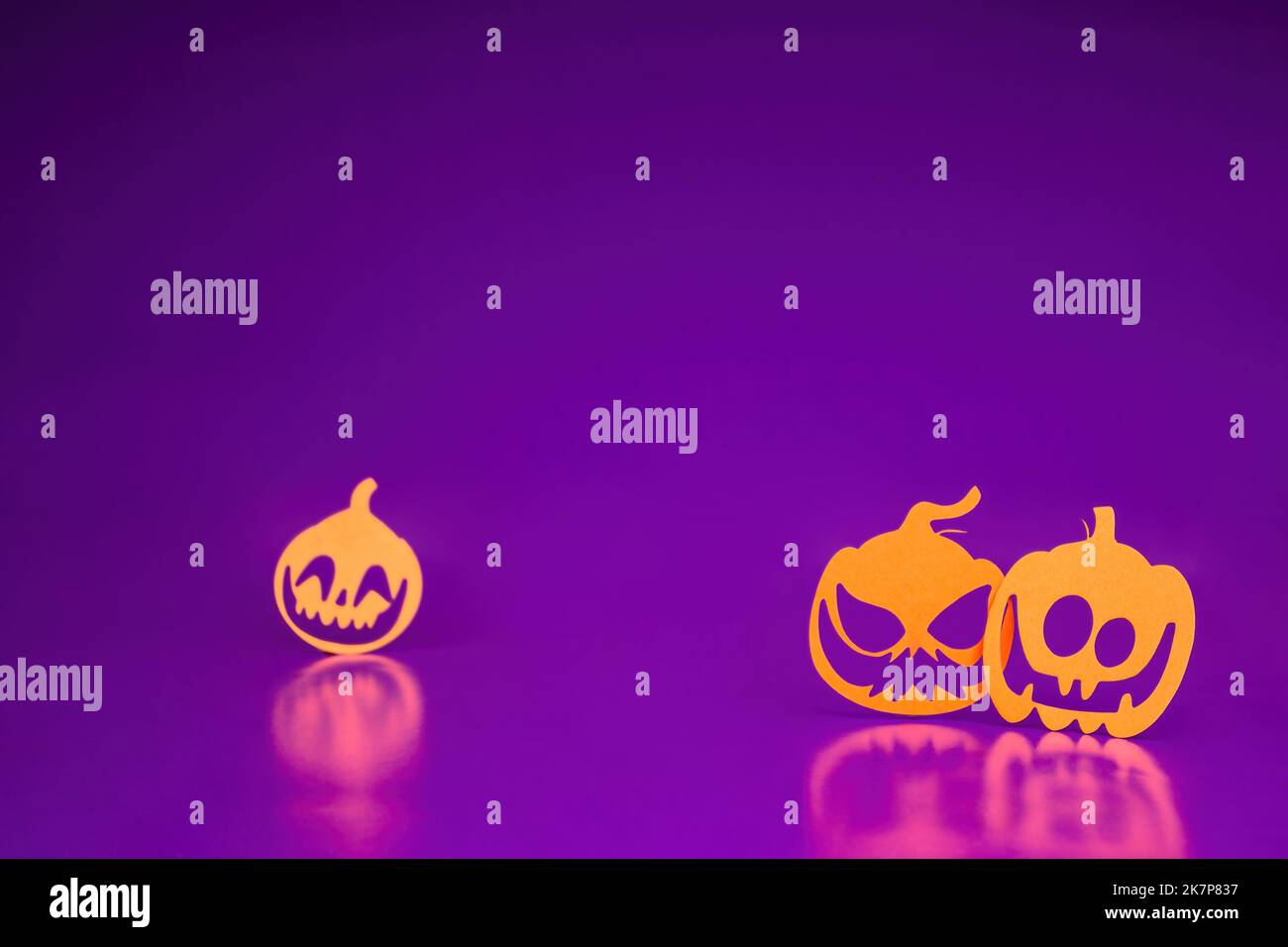 Tre zucche arrabbiate con taglio di carta arancione si trovano su uno sfondo viola. Concetto di Halloween, un sacco di spazio vuoto Foto Stock
