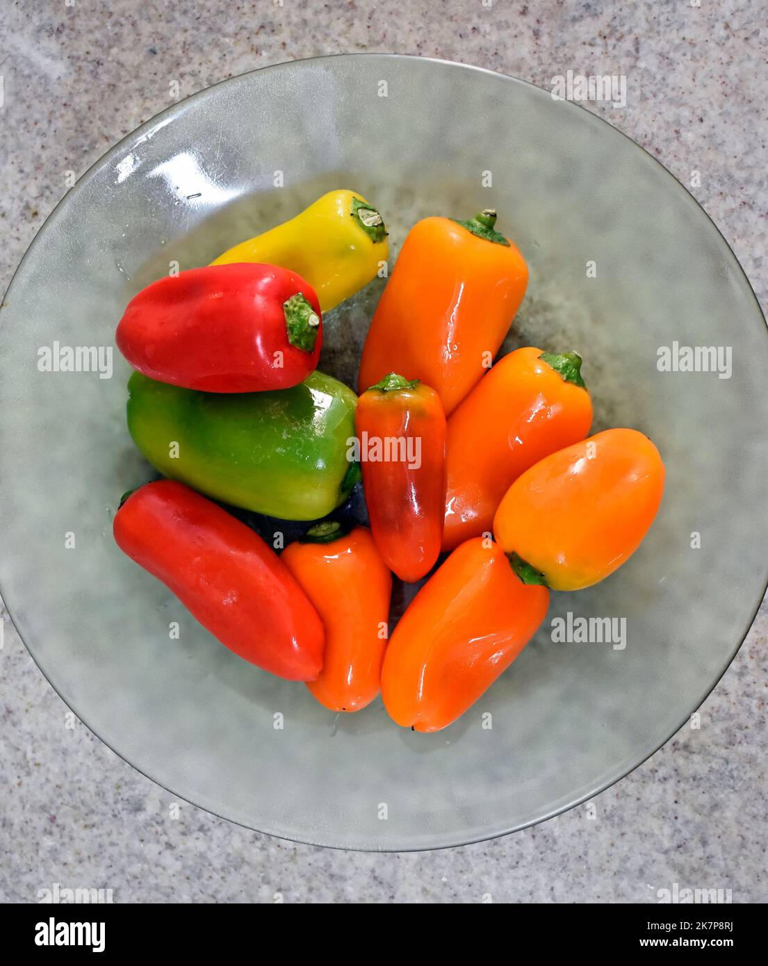 Mini peperoni su piatto di vetro su sfondo di granito Foto Stock