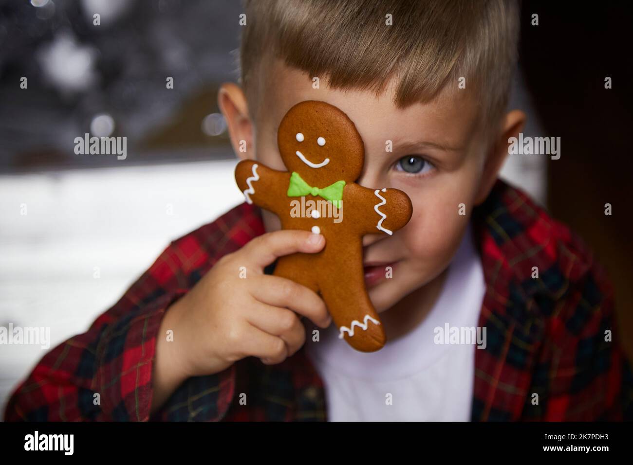 Cute cheerful toddler si nasconde dietro il pan di zenzero di Natale tra le decorazioni festive. Atmosfera accogliente casa per Capodanno. Buon umore. Bambino allegro Foto Stock