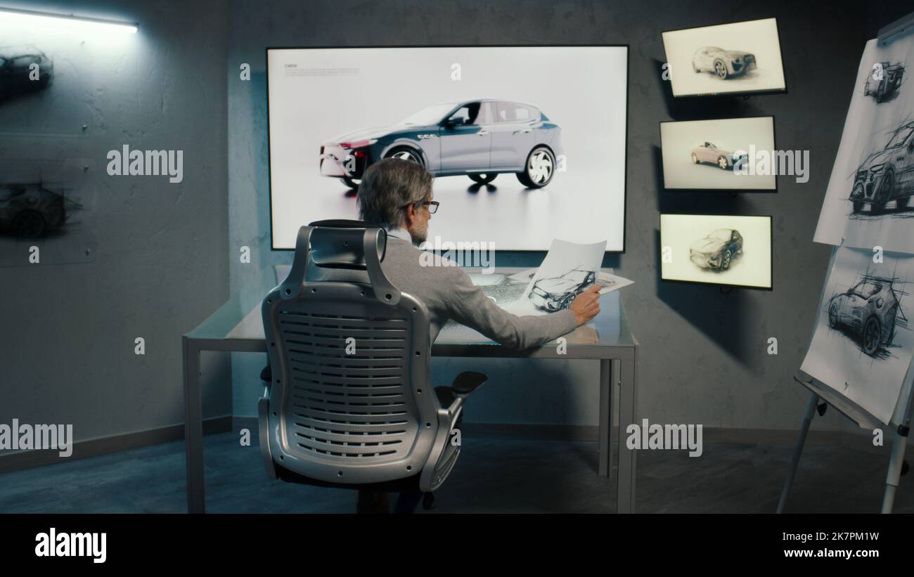 Vista posteriore di un grafico automobilistico disegna uno schizzo del modello prototipo di un'auto utilizzando una penna stilo in un innovativo laboratorio ad alta tecnologia. Industria automobilistica. Moderno monolocale con LED. Foto Stock