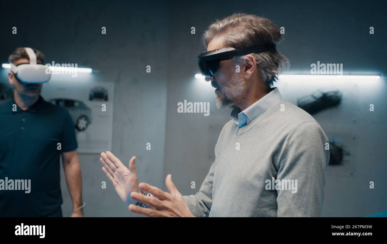 Due ingegneri professionisti del settore automobilistico che indossano occhiali per realtà virtuale parlano della produzione di veicoli mentre si trovano in un laboratorio di sviluppo high tech. Analisi e miglioramento della progettazione di automobili. Foto Stock