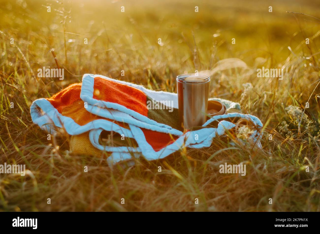 Tazza termica di tè caldo su una mano maglia coperta colorata sulla collina al tramonto Foto Stock