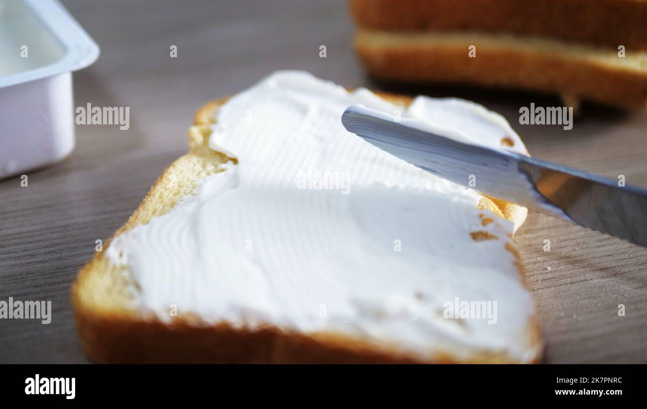 Coltello che sparge il burro su un pezzo di pane, vista ravvicinata. Concetto di colazione o pranzo Foto Stock