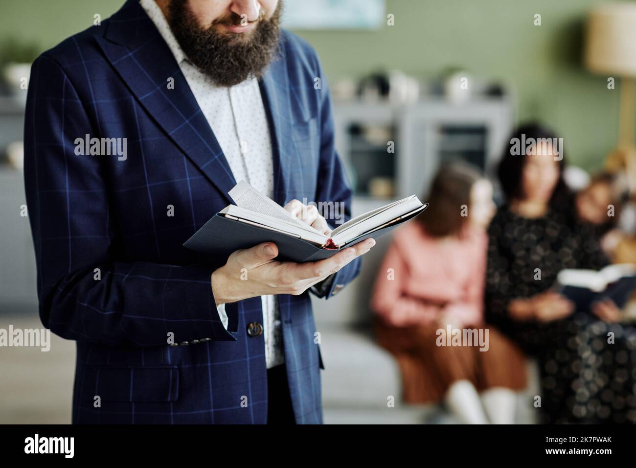 Ripresa ritagliata di un uomo ebreo barbuto che legge il libro a casa con la famiglia sullo sfondo, copia spazio Foto Stock