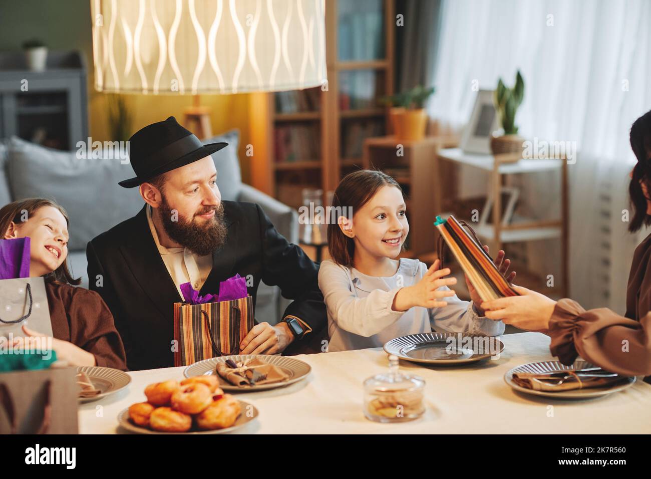 Accogliente ritratto della moderna famiglia ebraica che condivide regali al tavolo da pranzo mentre celebra le vacanze religiose Foto Stock