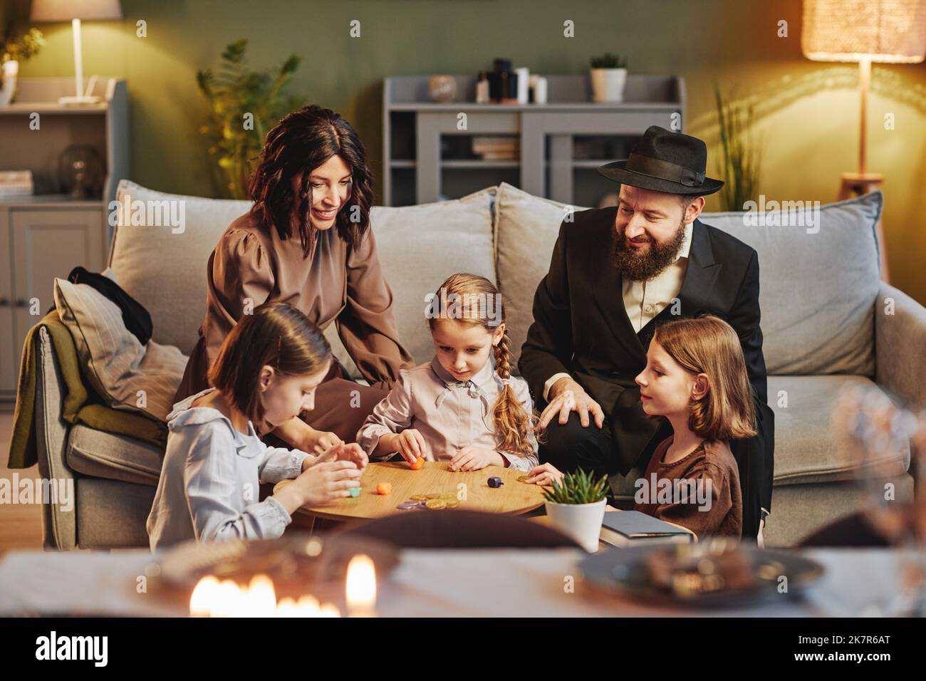 Ritratto della famiglia ebraica moderna che gioca tradizionale gioco dreidel in un ambiente accogliente casa Foto Stock