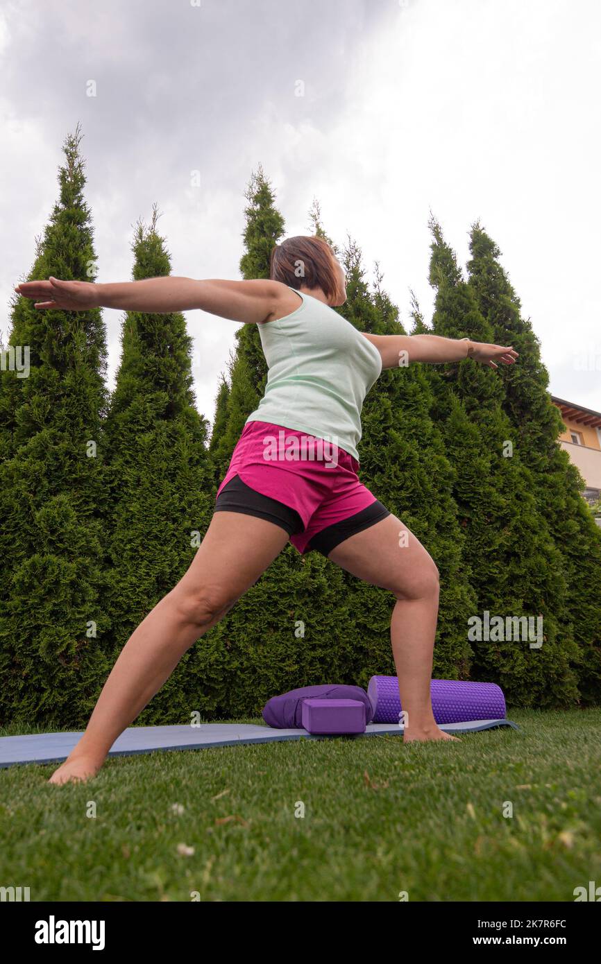 Donna che fa asana yoga per principianti su un tappetino in giardino in estate Foto Stock