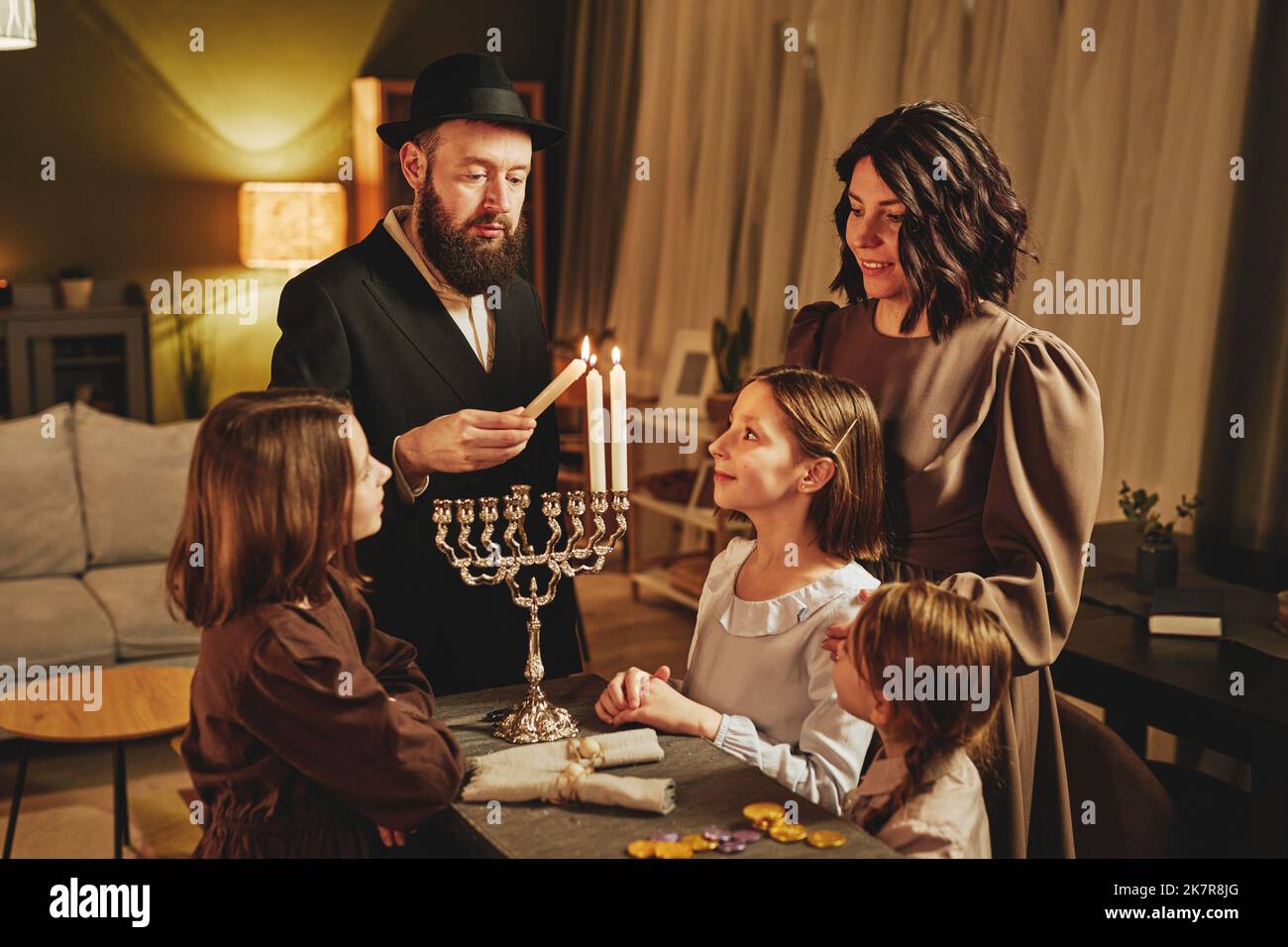 Ritratto della famiglia ebraica ortodossa che illumina insieme la candela di menorah durante la celebrazione di Hanukkah Foto Stock