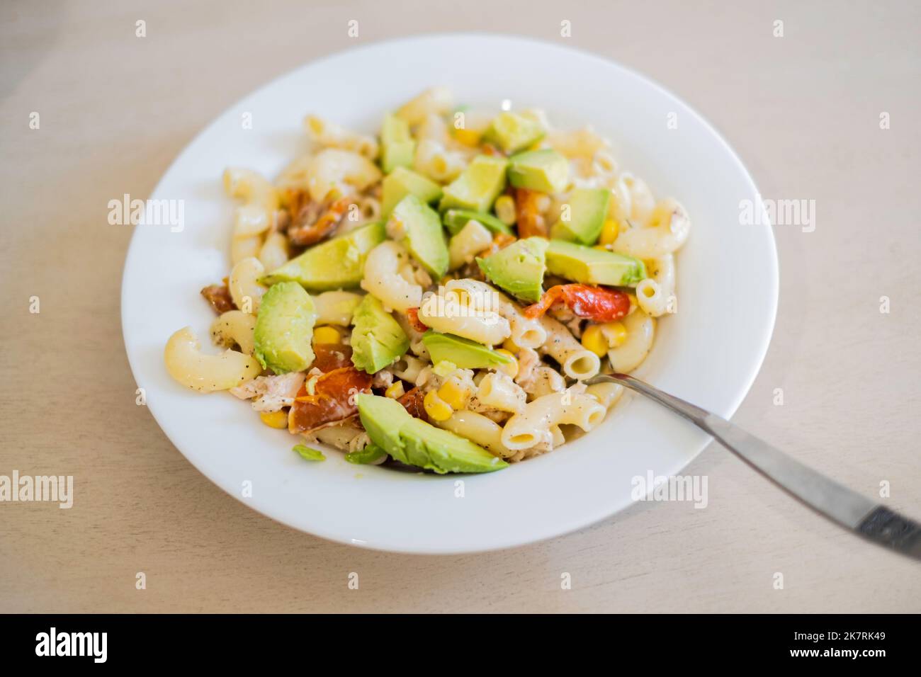 Un'insalata di pasta fredda composta da grandi maccheroni a gomito, avocado a fette, peperoni rossi tostati e mais in un piatto bianco sedette su un tavolo di legno. STATI UNITI Foto Stock