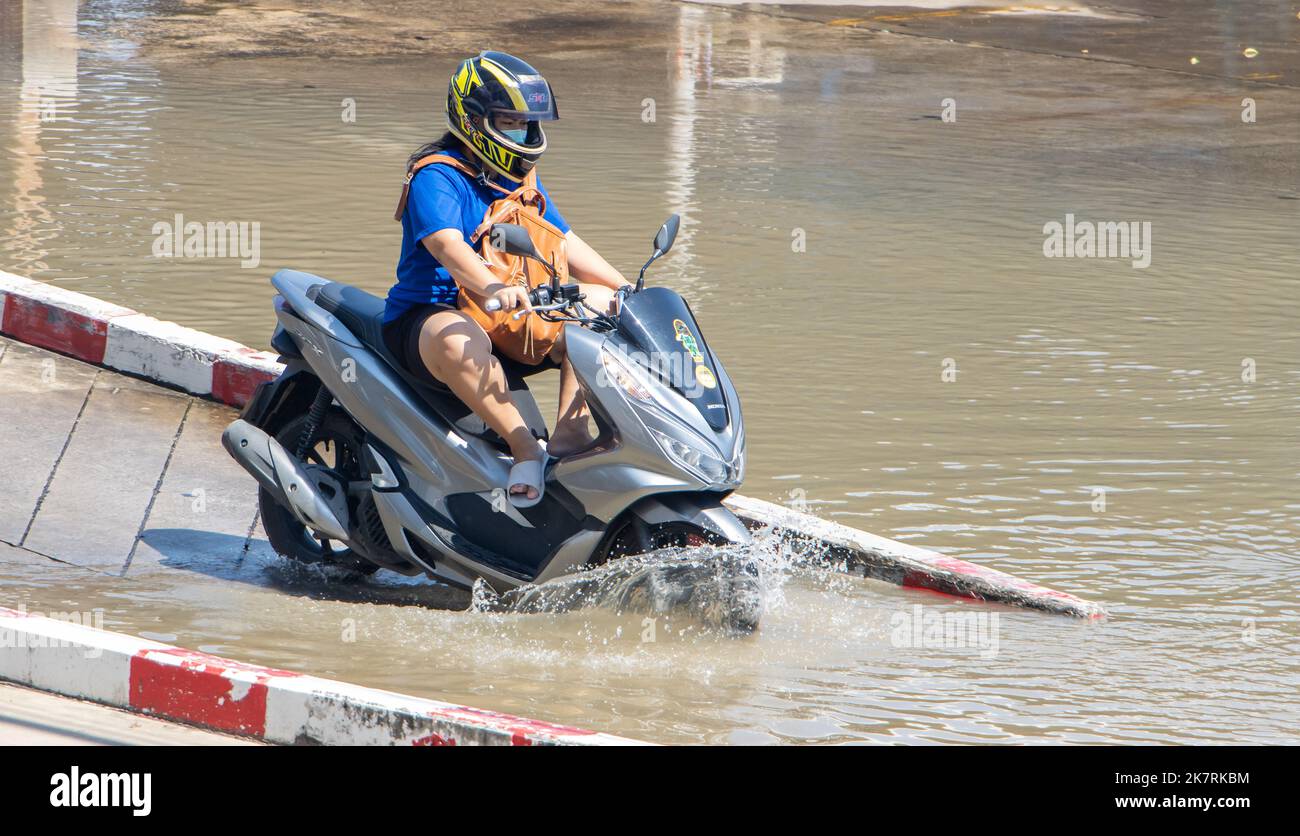 SAMUT PRAKAN, THAILANDIA, ottobre 13 2022, Un motociclista guida attraverso una strada allagata con i piedi in su Foto Stock