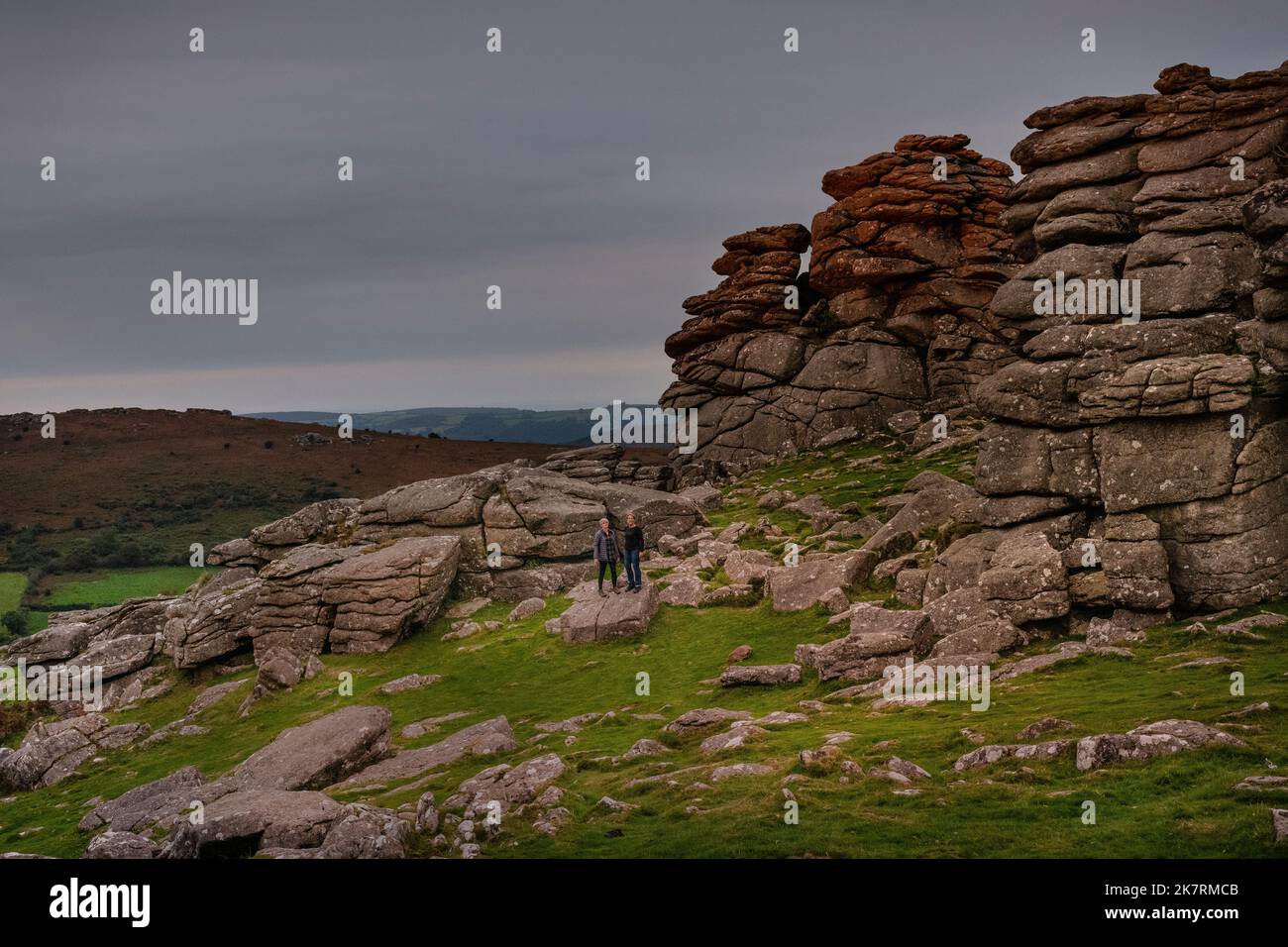 Hound Tor, dartmoor. Rocce di granito nel paesaggio due donne isolate nel paesaggio, trekking in piedi sulla formazione rocciosa. Foto Stock