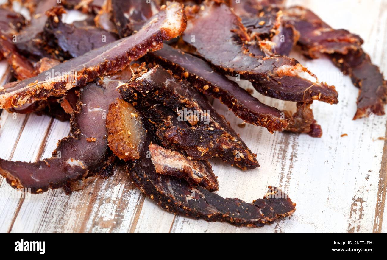 Affettato tradizionale biltong sudafricano o carne curata su superficie rustica di legno bianco Foto Stock