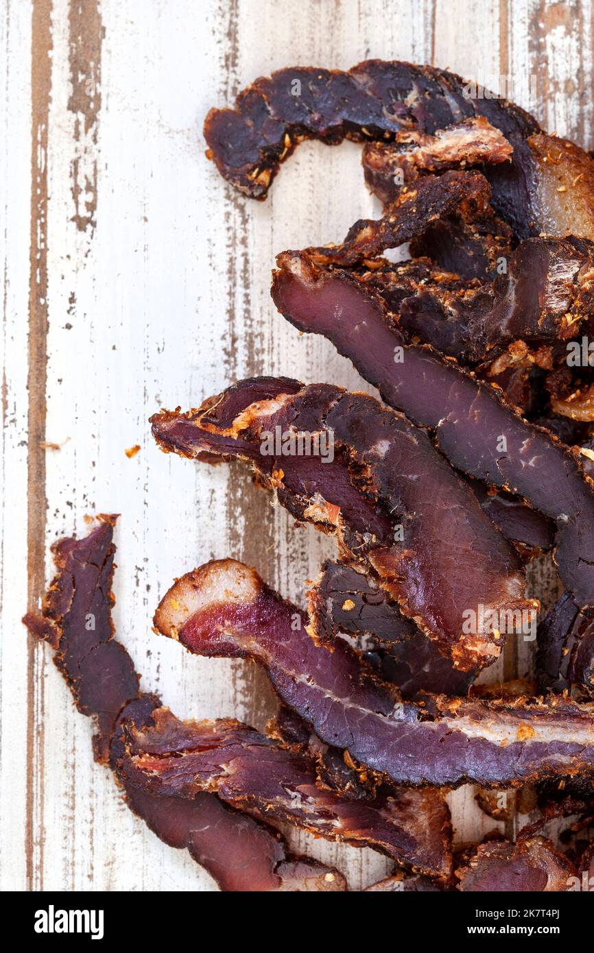 Affettato tradizionale biltong sudafricano o carne curata su superficie rustica di legno bianco Foto Stock