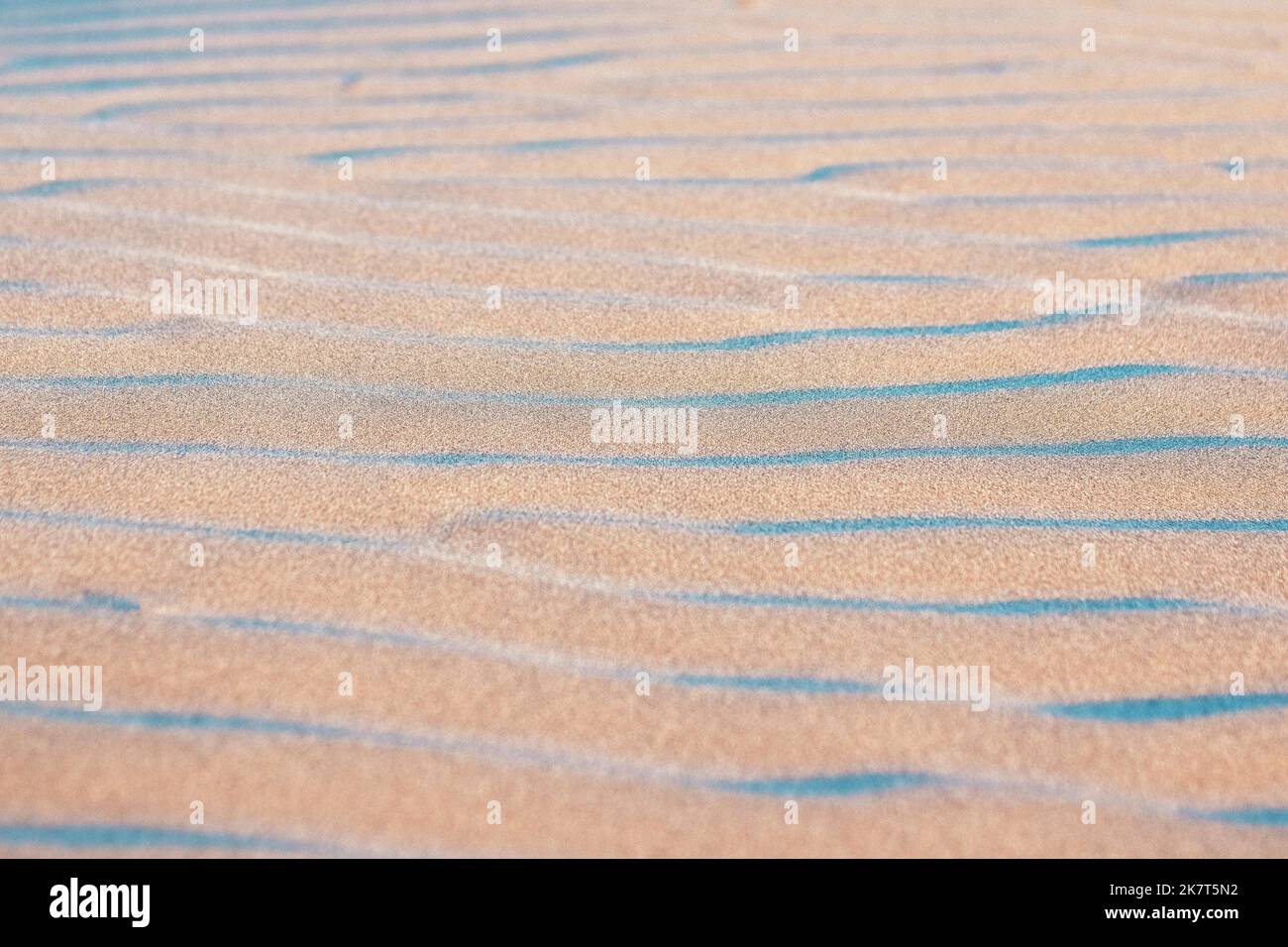 Le onde nella sabbia di una spiaggia dell'Oceano Pacifico creano un modello astratto in blu e rosa. Foto Stock