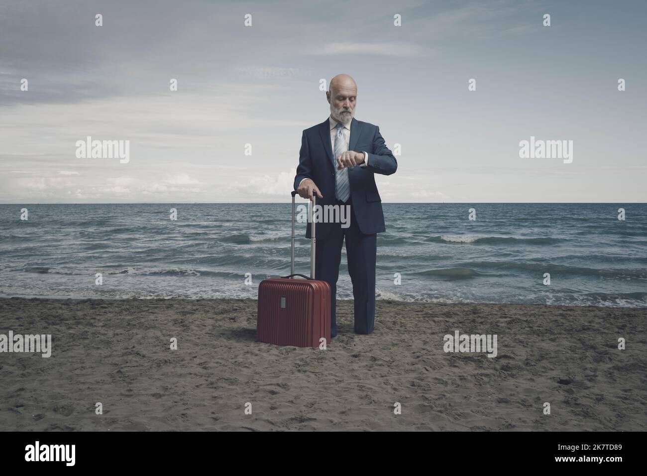 Uomo d'affari in viaggio in attesa di partire in spiaggia e controllare l'orario, è bloccato nella sabbia Foto Stock