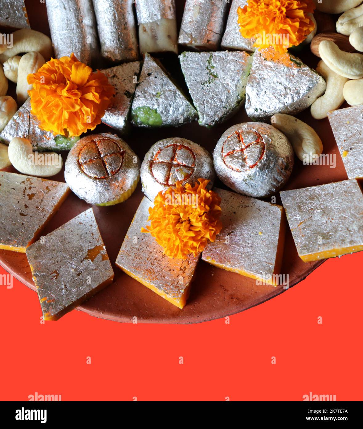Dolci indiani assortiti / frutta secca / fiore di marigold in un piatto di terracotta / argilla su sfondo rosso - Diwali / Deepavali festival Foto Stock