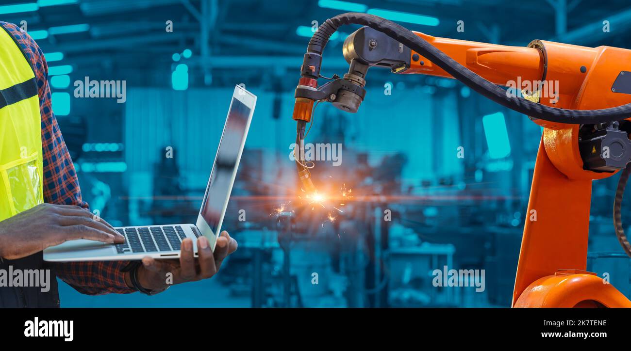 Ingegnere che utilizza computer portatile controllo di programma saldatura del braccio robotico con sistema di automazione ai in avanzata fabbrica moderna di metallo.industria 5,0 fabr Foto Stock