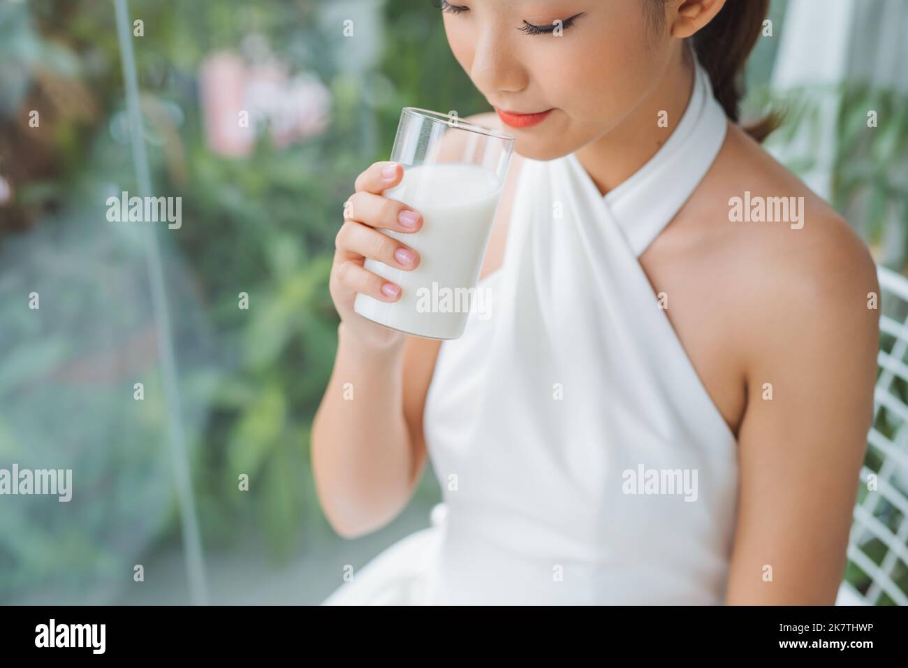 Bella giovane donna asiatica che beve latte fresco la mattina a casa con faccia felice. Foto Stock