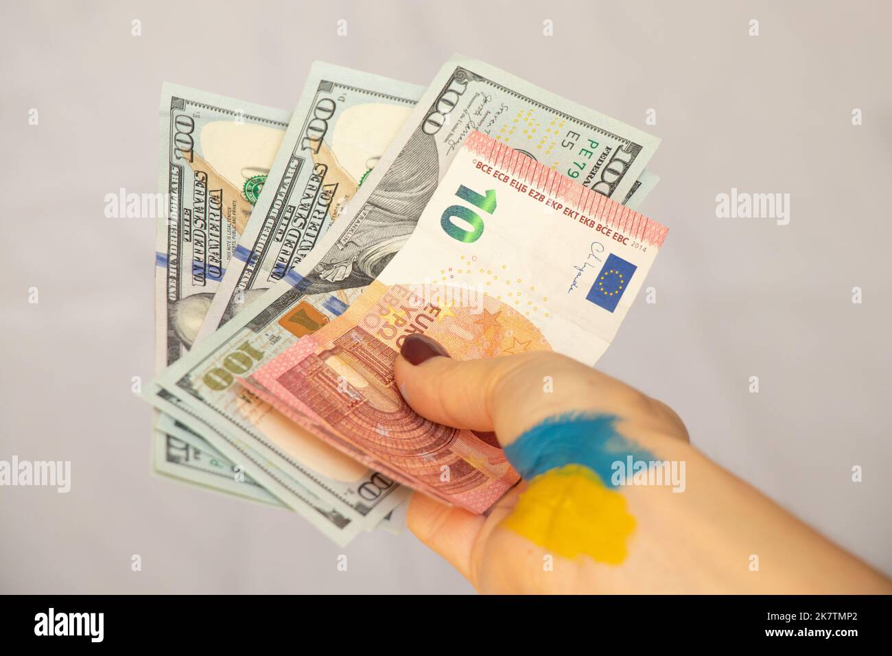 Dollari ed euro nelle mani di una donna Ucraina con una bandiera dipinta dell'Ucraina su un fondo isolato, una mano d'aiuto per l'Ucraina Foto Stock