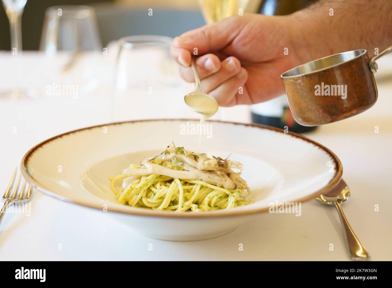 Persona che versa la salsa sul piatto di pasta servito su piatto bianco Foto Stock