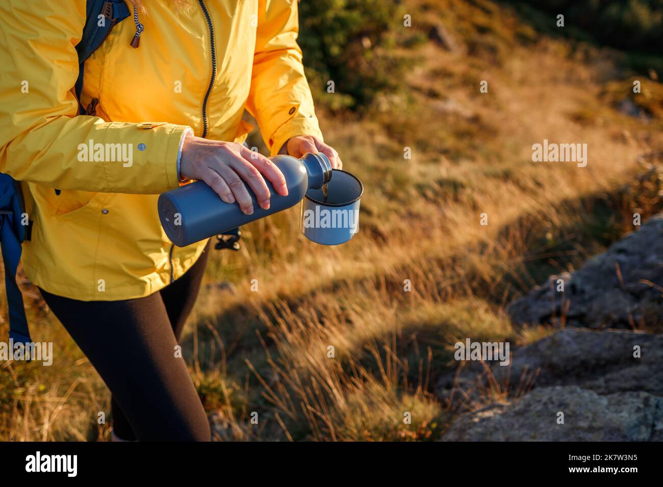 L'escursionista sta versando la bevanda calda dai thermos nella tazza di viaggio in montagna. Rinfresco durante il trekking nella natura. Donna che indossa abbigliamento sportivo Foto Stock