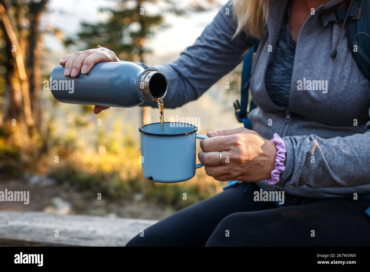Donna che versa la bevanda del tè nella tazza di viaggio. Rinfresco durante le escursioni nella foresta Foto Stock