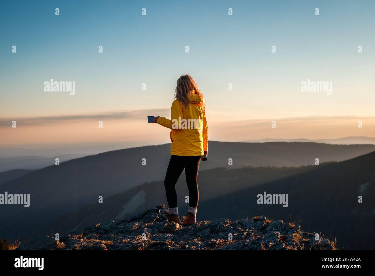 Donna escursionista con bevanda calda godendo il tramonto e la vista sulla catena montuosa. Relax durante le escursioni all'aperto Foto Stock