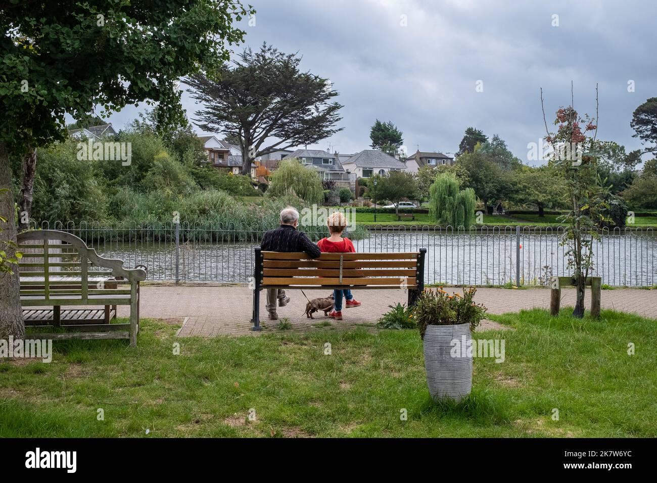 Una coppia seduta su una panca con il loro cane che guarda Trenance Boating Lake a Newquay in Cornovaglia nel Regno Unito. Foto Stock