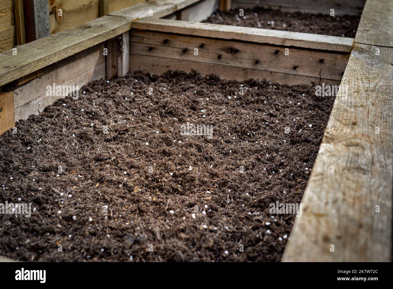 Primo piano di un grande contenitore in legno per la piantatrice di verdure in giardino riempito di terreno pronto per la piantatura di semi e piante. Foto Stock