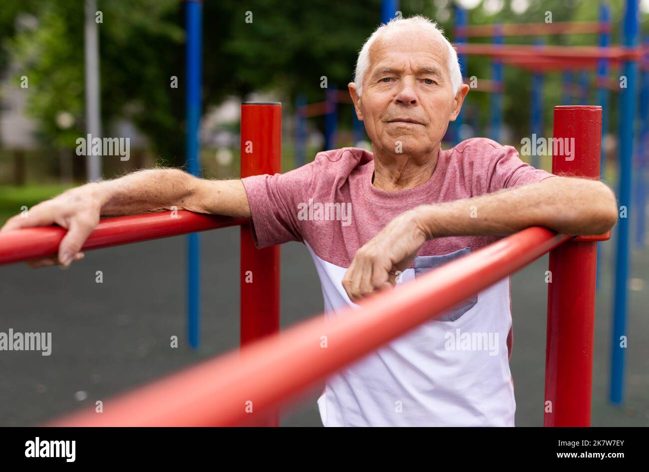 L'uomo sportivo più anziano esegue varie esercitazioni sulle barre irregolari nel parco Foto Stock