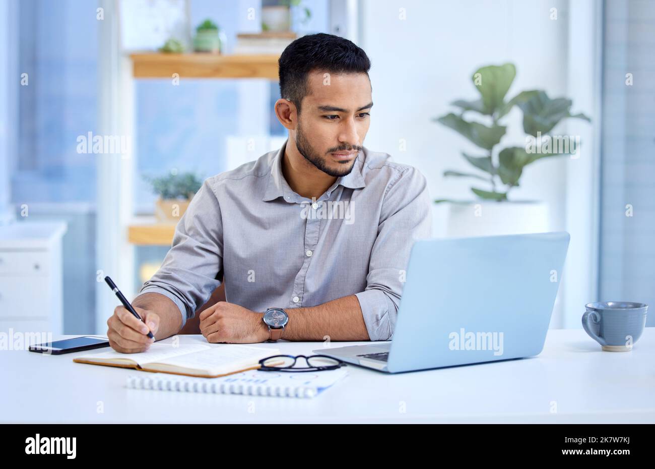 Facendo una certa ricerca sulle ultime tendenze di mercato. un giovane uomo d'affari che scrive appunti mentre lavora su un computer portatile in ufficio. Foto Stock