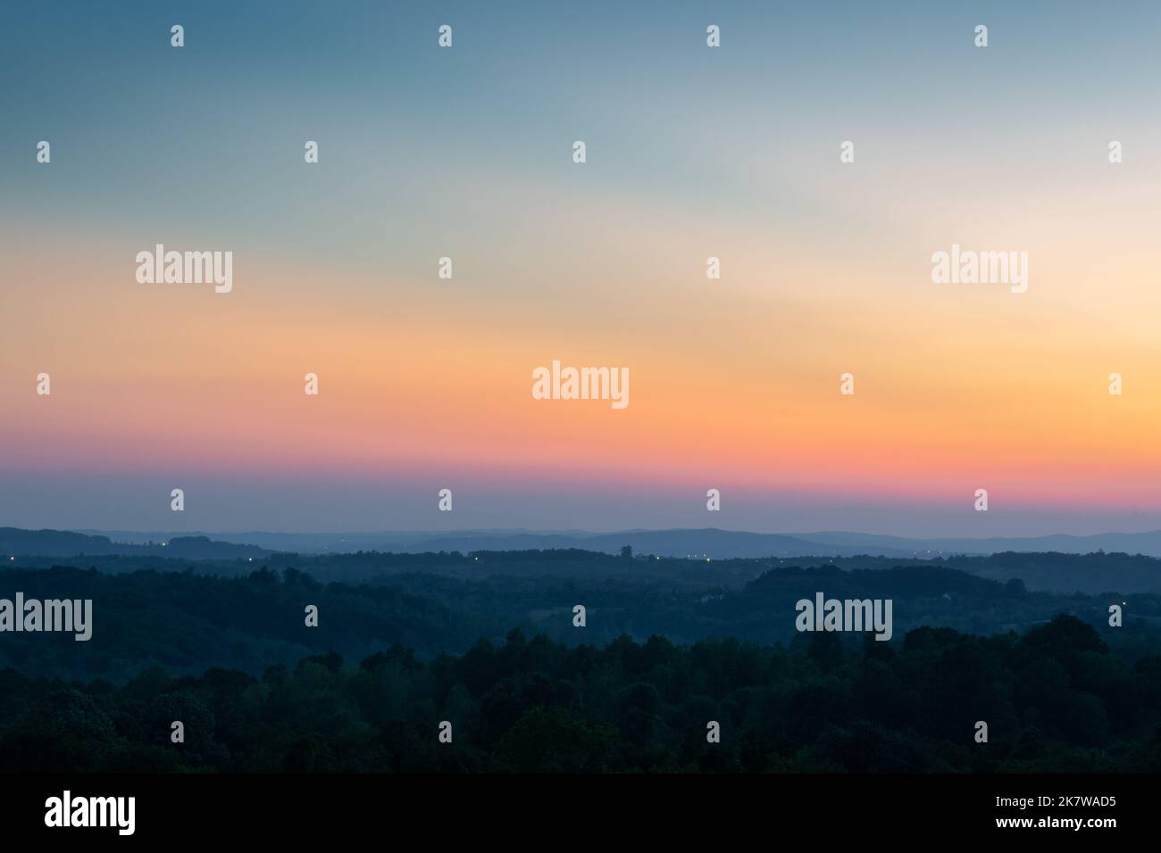 Strati di collina separati da foschia e vibrante bagliore nel cielo sopra l'orizzonte al crepuscolo, paesaggio rurale collinare con l'ultima luce sul cielo limpido Foto Stock