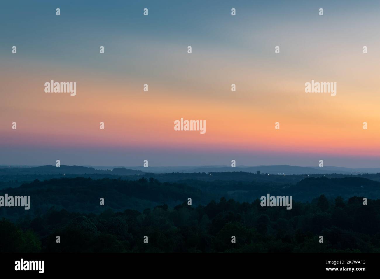 Strati di collina separati da foschia e vibrante bagliore nel cielo sopra l'orizzonte al crepuscolo, paesaggio rurale collinare con l'ultima luce sul cielo limpido Foto Stock