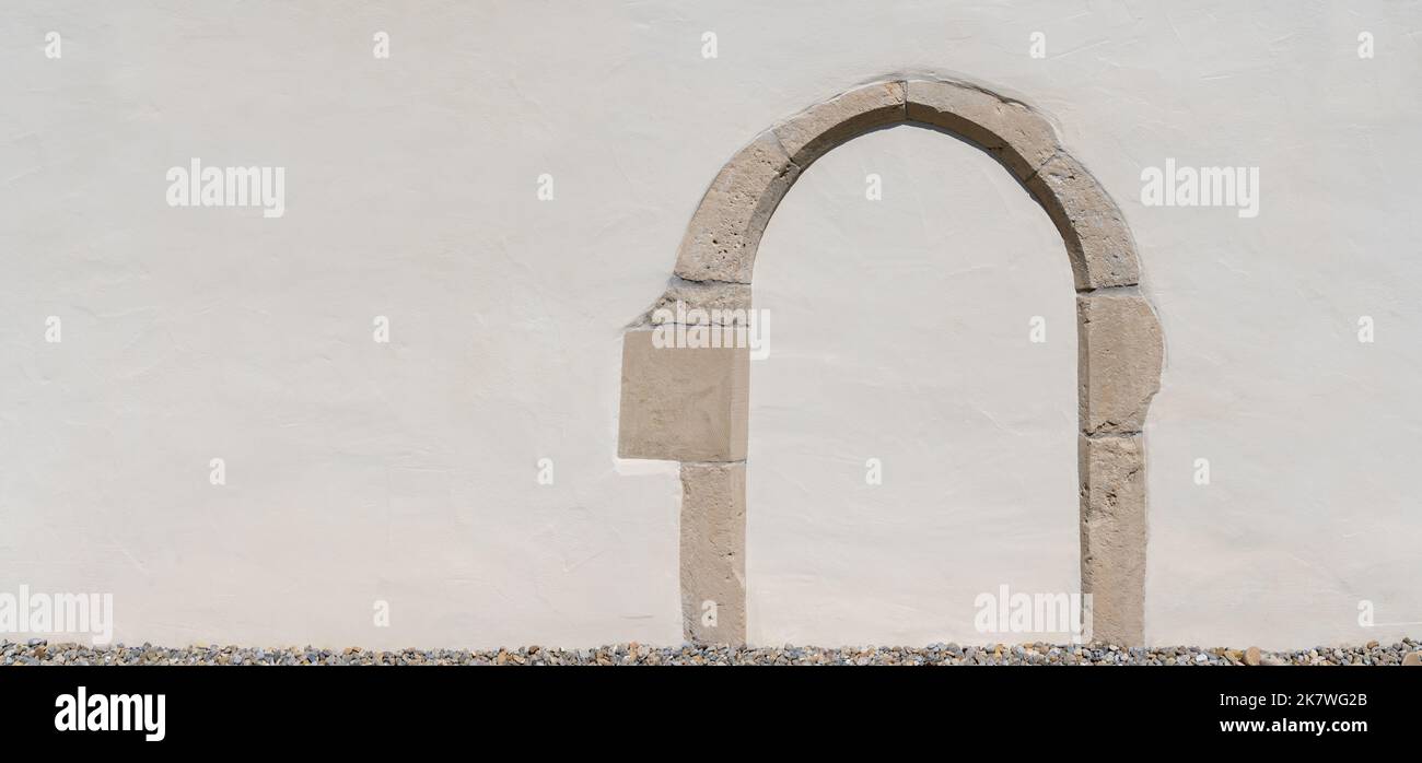 Vecchio muro intonacato bianco con un arco lavorato in pietra Foto Stock