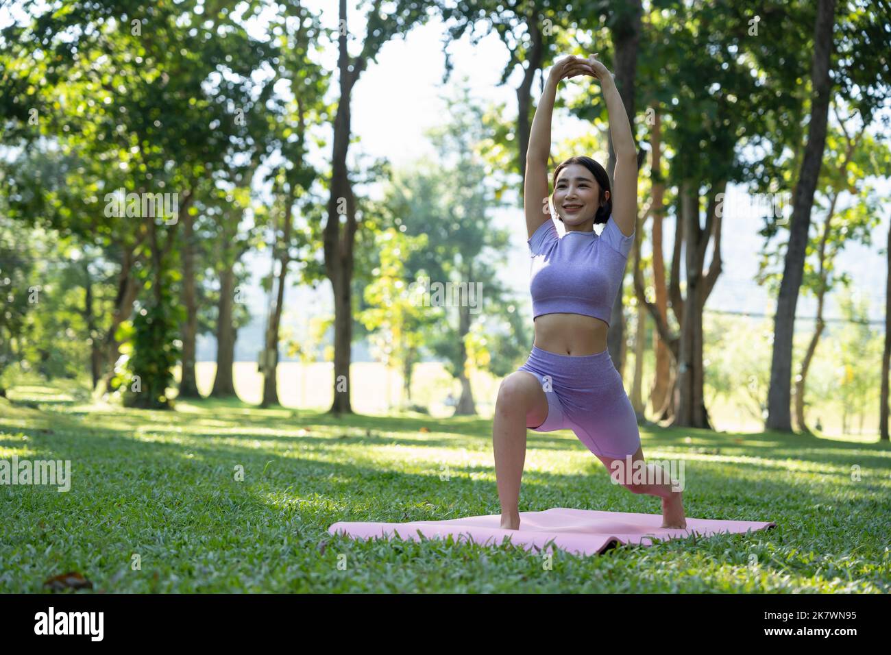 Persone sane e mature che fanno yoga al parco. Donna asiatica che si esercita su erba verde con tappetino yoga. Foto Stock