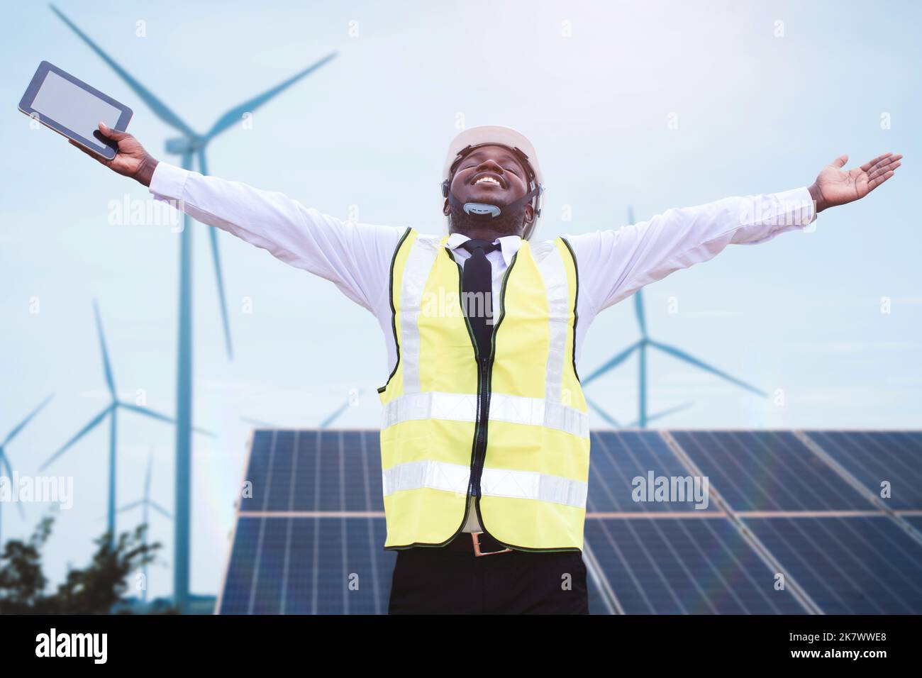 Il manager di un ingegnere africano di successo ha in mano un tablet con turbine solari fotovoltaiche ed eoliche che generano centrali elettriche. Concetto di s Foto Stock