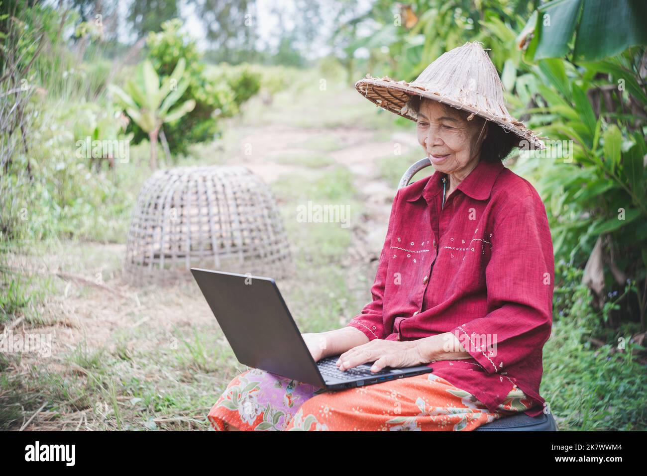 Una donna asiatica anziana che impara e usa un computer portatile all'interno di una fattoria con un sorriso e felicità Foto Stock