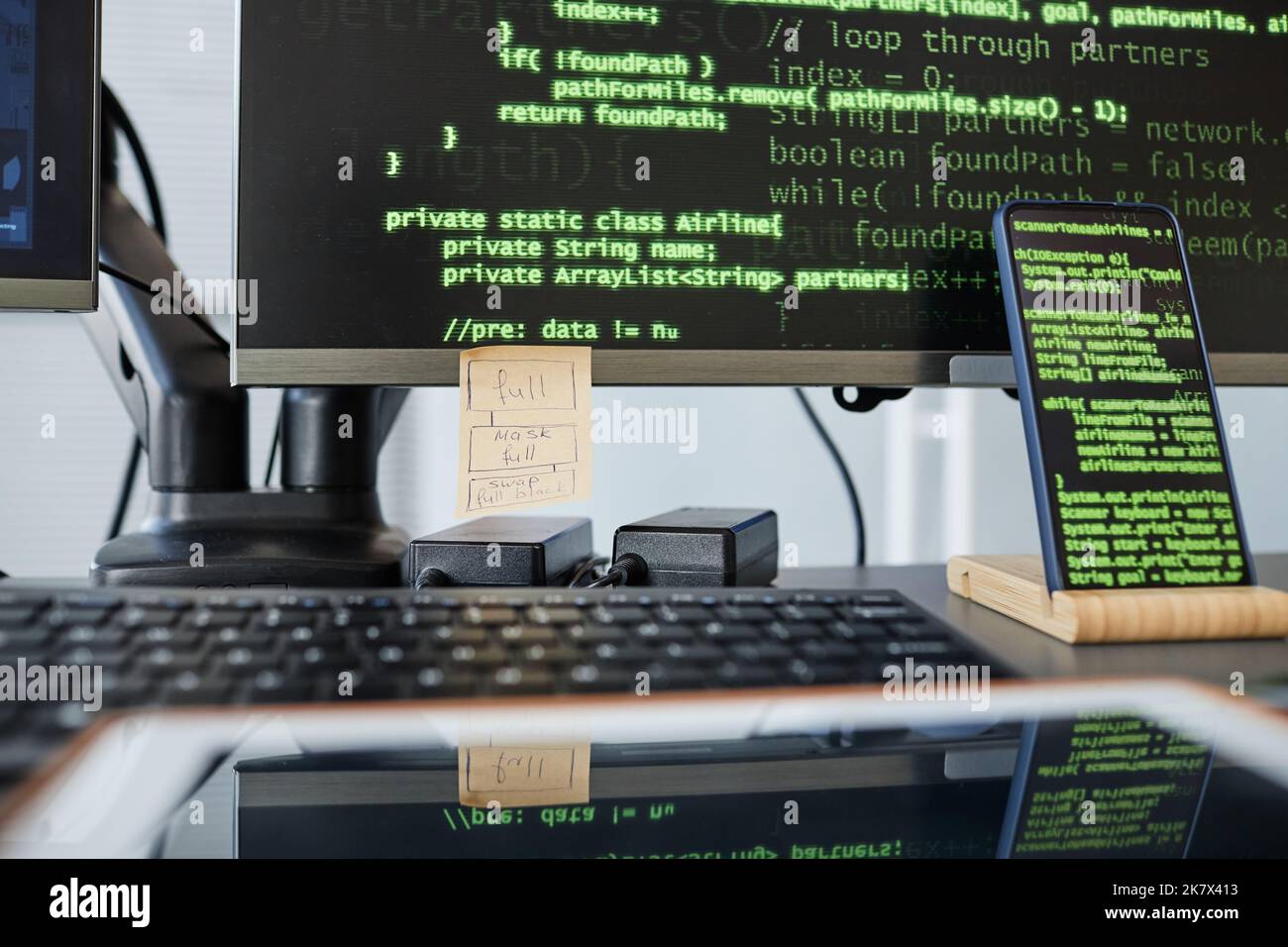 Primo piano dell'ambiente di lavoro dei programmatori con la tastiera del computer e le righe di codice verdi sullo schermo Foto Stock