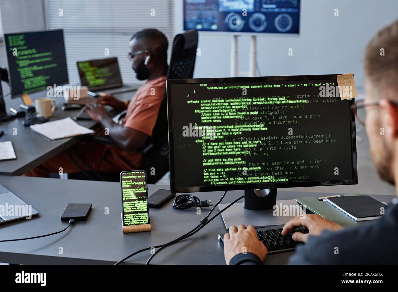 Immagine di sfondo dell'ufficio sviluppo software con righe di codice verdi sullo schermo del computer, spazio copia Foto Stock