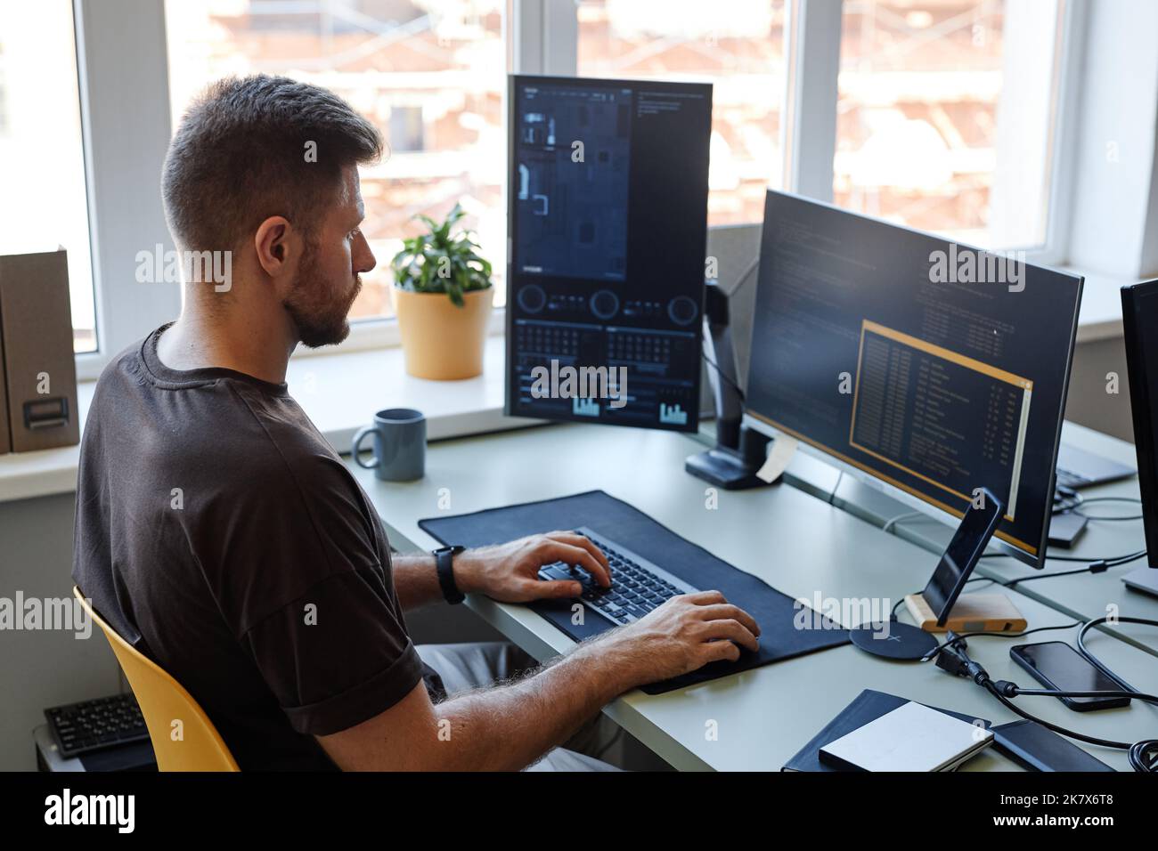Ritratto ad angolo alto di un giovane software engineer che scrive codice sul posto di lavoro con più schermi di computer Foto Stock
