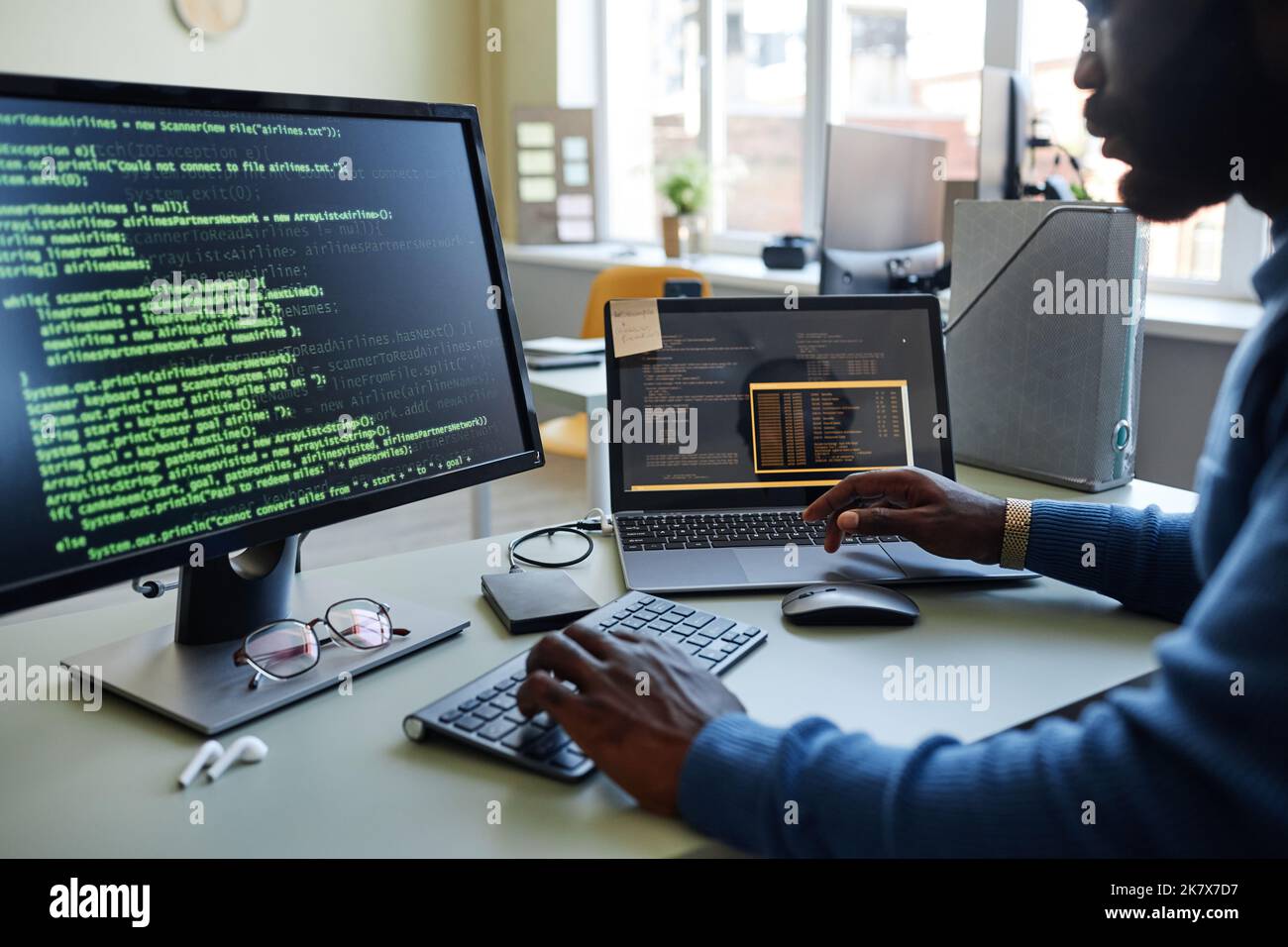 Primo piano dello sviluppatore di software nero che scrive codice sul luogo di lavoro in ufficio con più dispositivi Foto Stock