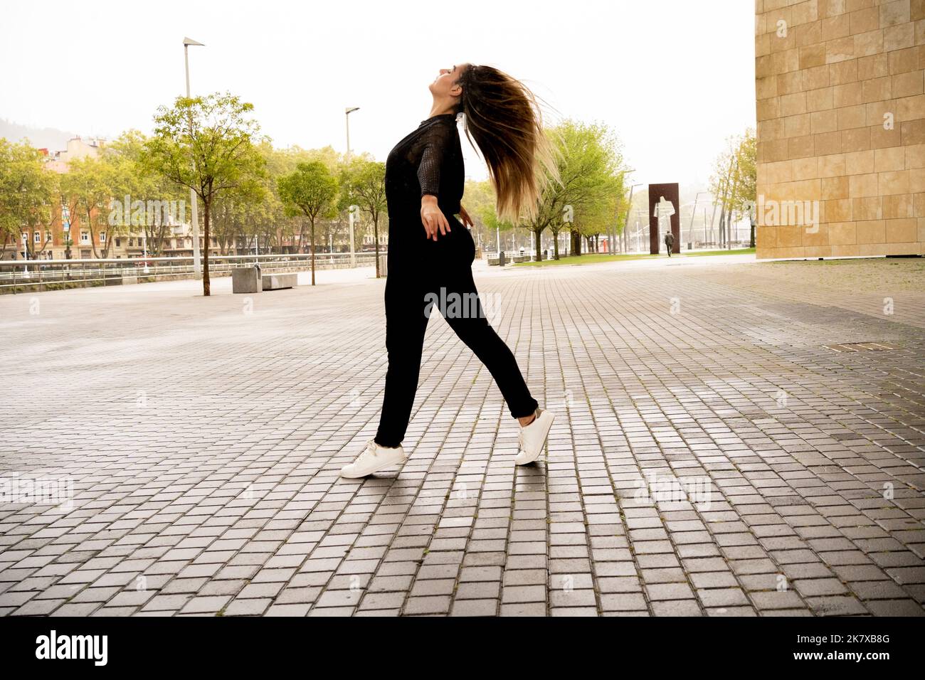 giovane donna che fa balletto figura sulla strada sotto la pioggia Foto Stock