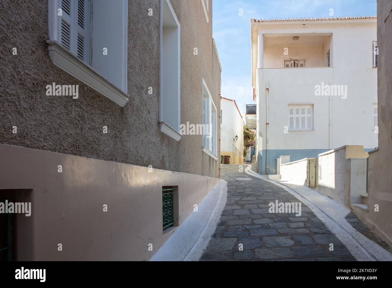 Grecia, Cicladi. Andros isola, Chora città. Vicolo di ciottoli di fronte alle tradizionali mura delle case, sotto il sole greco e lo sfondo blu del cielo. Foto Stock