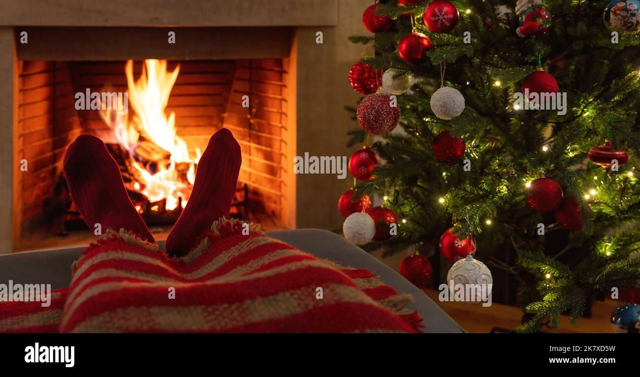 Uomo che si rilassa al camino in fiamme, albero di Natale decorazione. Calze calde e coperta, sfondo interno casa vacanza inverno. Foto Stock