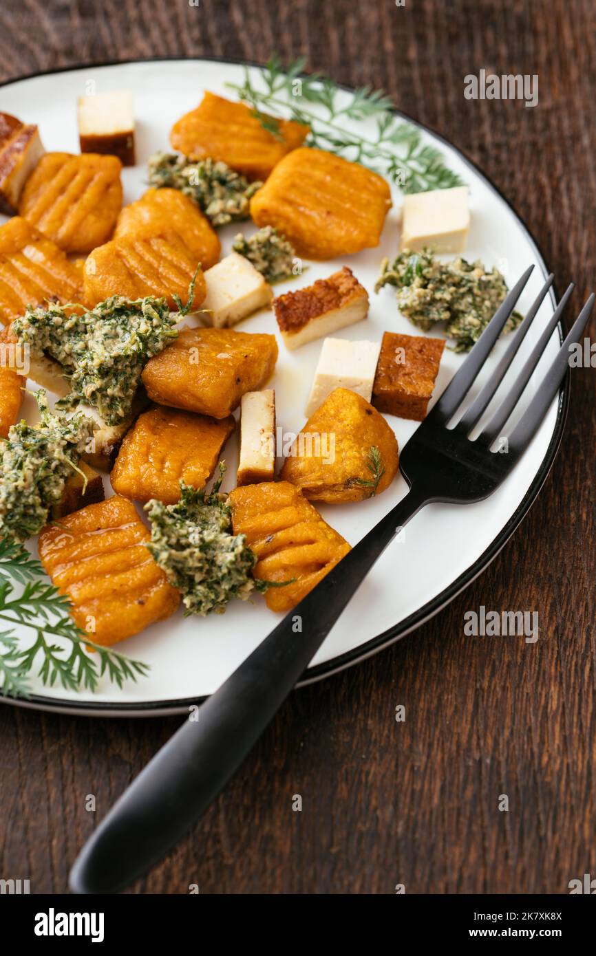 Piatto con gnocchi di carote fatti in casa con pesto sulla carota e tofu affumicato. Foto Stock