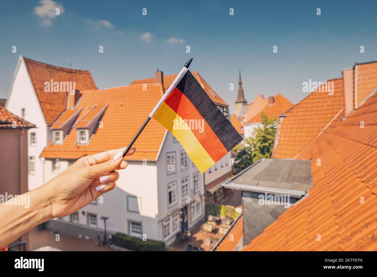 Una mano che tiene una bandiera tedesca contro i tetti arancioni della città vecchia di Osnabruck. Patriottismo e feste tradizionali Foto Stock