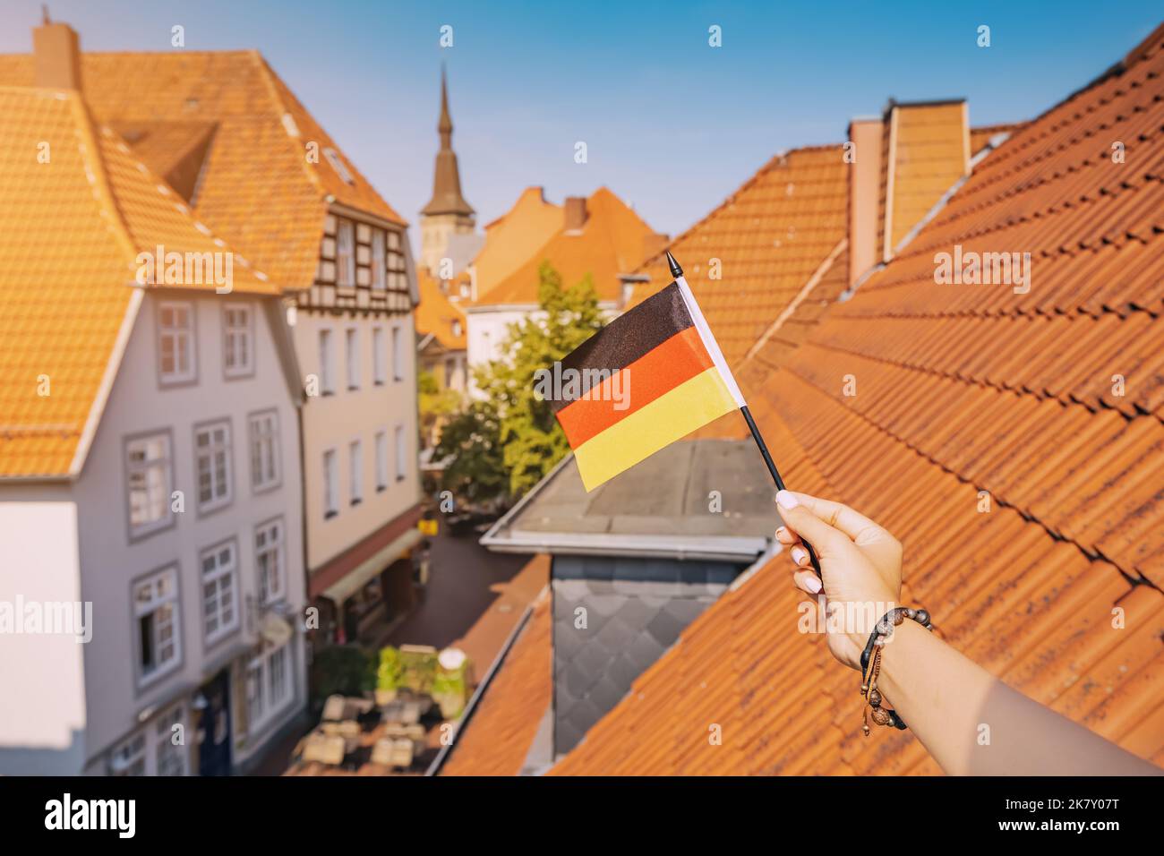 Una mano che tiene una bandiera tedesca contro i tetti arancioni della città vecchia di Osnabruck. Patriottismo e feste tradizionali Foto Stock
